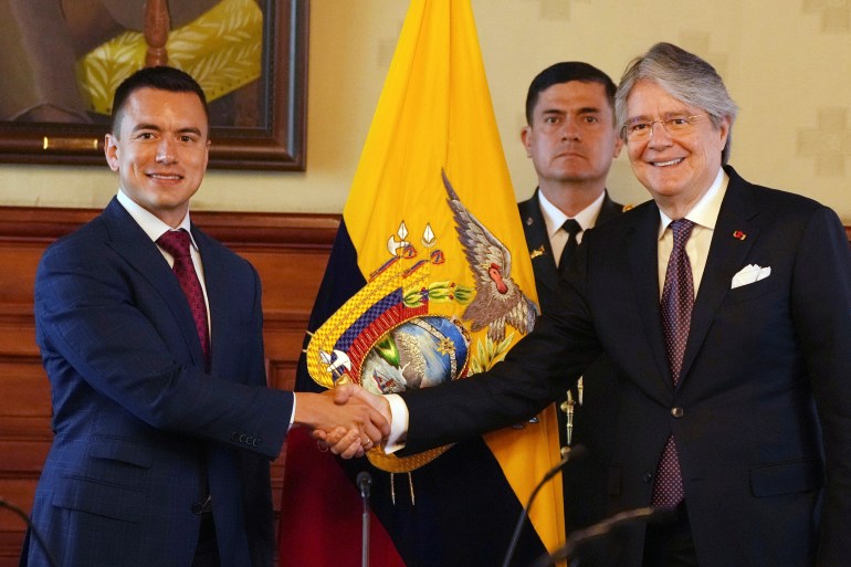 Daniel Noboa podaje rękę Guillermo Lasso.  Za nimi flaga Ekwadoru i mężczyzna w garniturze stojącym pod ścianą.