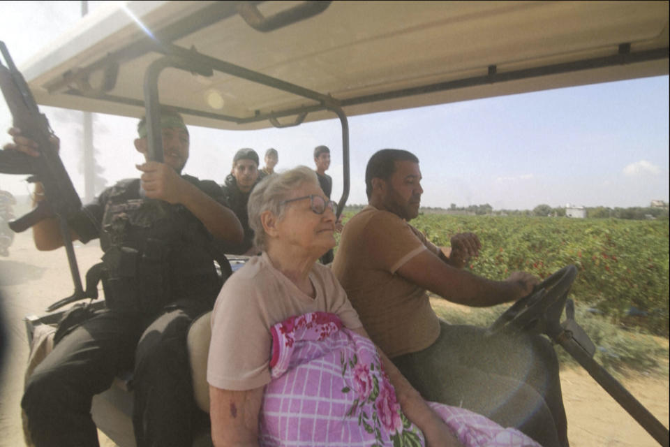 Starsza kobieta o siwych włosach jedzie wózkiem golfowym z uzbrojonym żołnierzem.