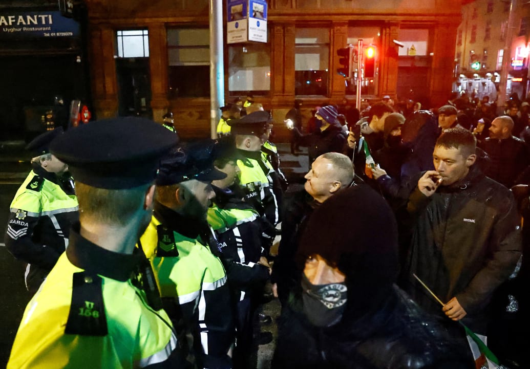 Ludzie stoją przed policją w pobliżu miejsca podejrzenia pchnięcia nożem, w wyniku którego niewiele dzieci zostało rannych, Dublin, Irlandia, 23 listopada 2023 r.