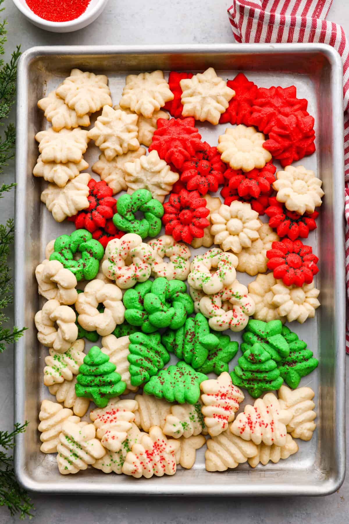 Spritz ciasteczka na blasze do pieczenia.  Niektóre są barwione na zielono lub czerwono.  Mają kształt choinek i płatków śniegu.