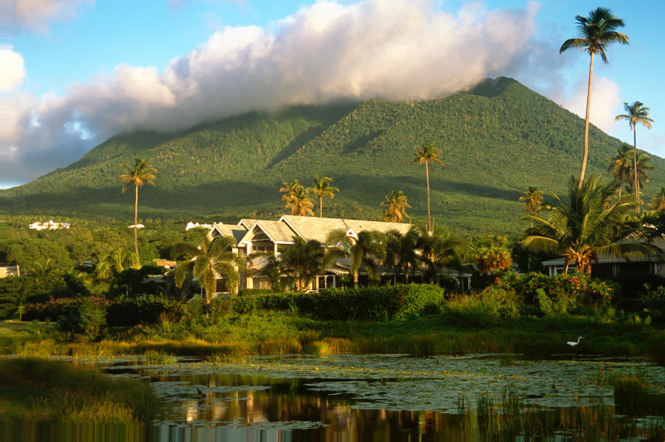 Wygasły wulkan Nevis Peak widziany z jeziora, z domami, palmami i puszystą chmurą na szczycie, Nevis