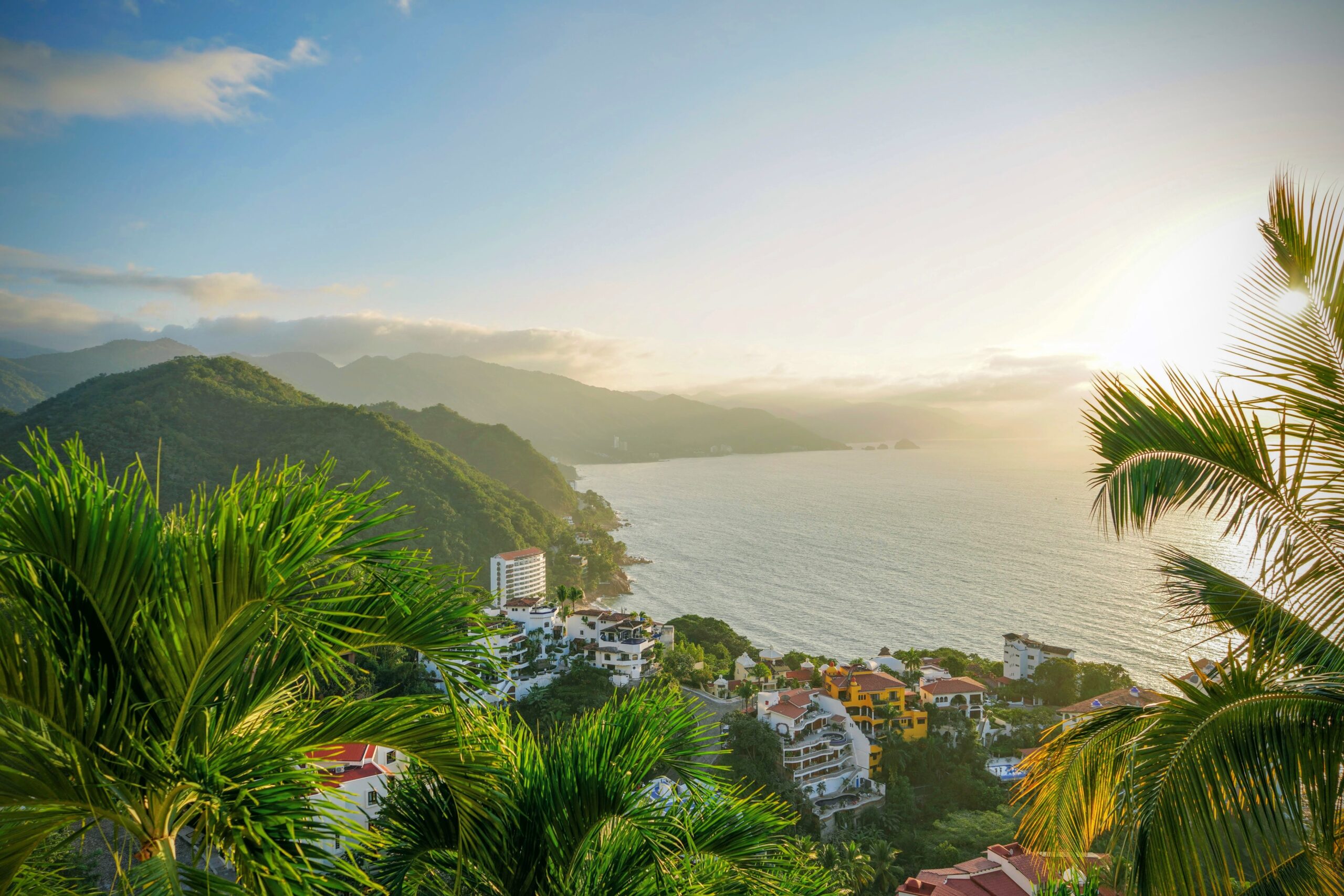 Podróżni powinni rozważyć wycieczkę do Puerto Vallarta na bezpieczną, ale ekscytującą wycieczkę tropikalną.  Na zdjęciu: wybrzeże Puerto Vallarta podczas zachodu słońca z tętniącym życiem lasem i miastem 