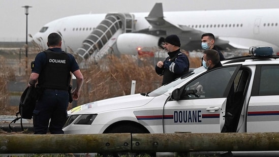 Francuscy celnicy stoją obok samochodu celnego z Airbusem A340 w tle, który od 21 grudnia unieruchomiony jest na asfalcie w związku z podejrzeniem "handel ludźmi"na lotnisku w Vatry.  (AFP)