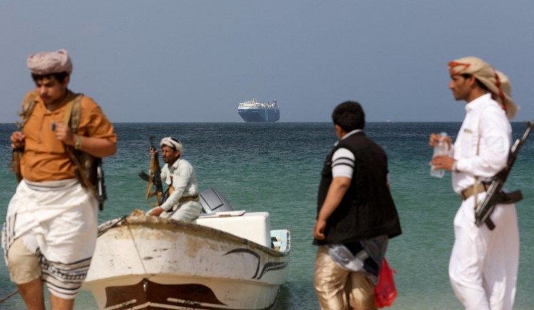Uzbrojeni mężczyźni stoją na plaży, gdy statek handlowy Galaxy Leader, przejęty przez jemeńskich Houthi w zeszłym miesiącu, jest zakotwiczony u wybrzeży al-Salif w Jemenie, 5 grudnia 2023 r. [REUTERS/Khaled Abdullah/File]