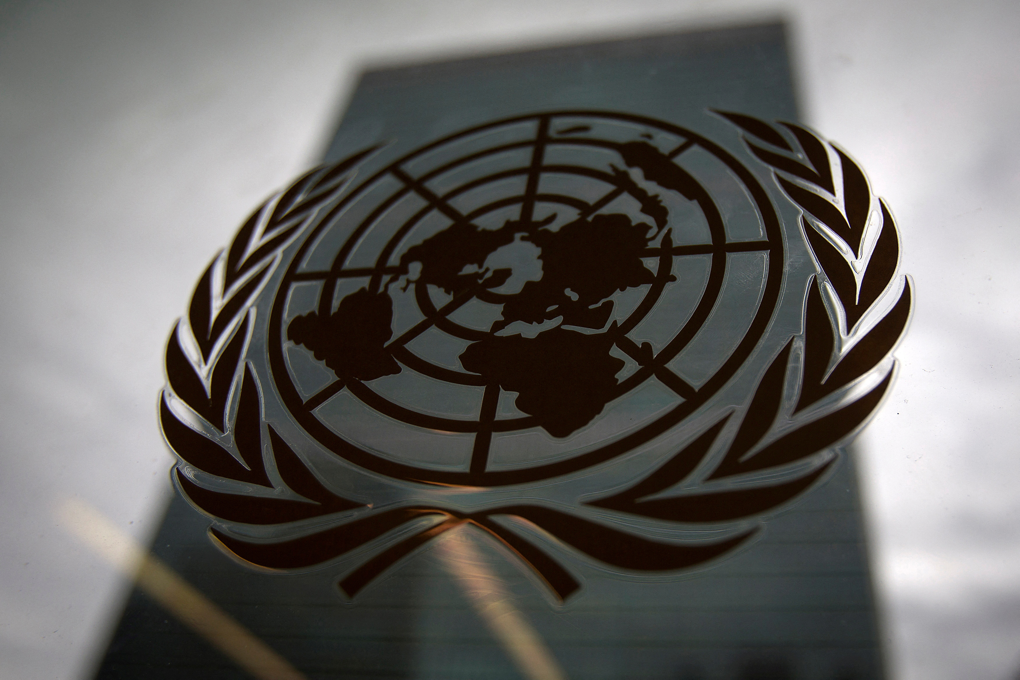 Budynek siedziby Organizacji Narodów Zjednoczonych jest pokazany przez okno z logo ONZ na pierwszym planie w dzielnicy Manhattan w Nowym Jorku