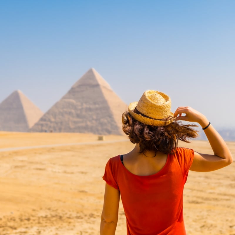 kobieta w czerwonym topie patrząca na piramidy w oddali w Egipcie