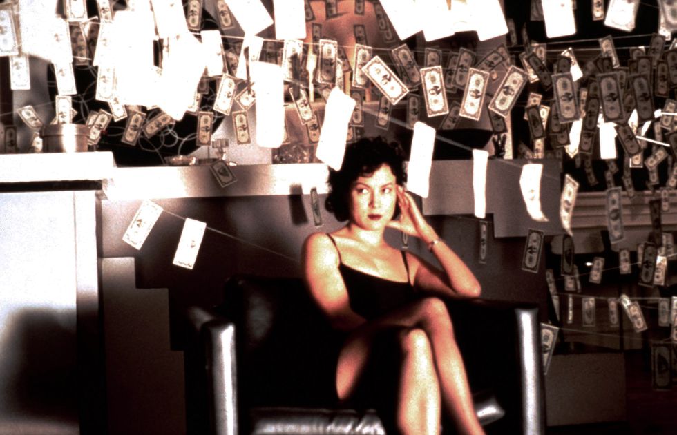 brunetka siedząca w pokoju wypełnionym pieniędzmi wiszącymi na sznurkach do bielizny
