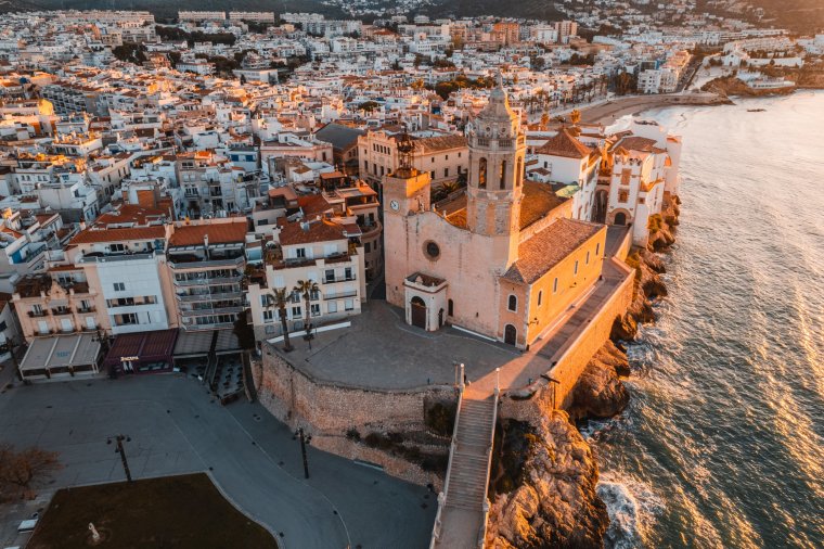 Widok z lotu ptaka na Sitges i Iglesia de San Bartolom??  y Santa Tecla o wschodzie słońca.  Najbardziej uderzającym zabytkiem Sitges jest XVII-wieczny kościół parafialny, dumnie wznoszący się na skalistym zboczu otoczonym morzem, oddzielającym główną plażę o długości 2 km na południowym zachodzie od mniejszych piaszczystych pasm na północnym wschodzie.