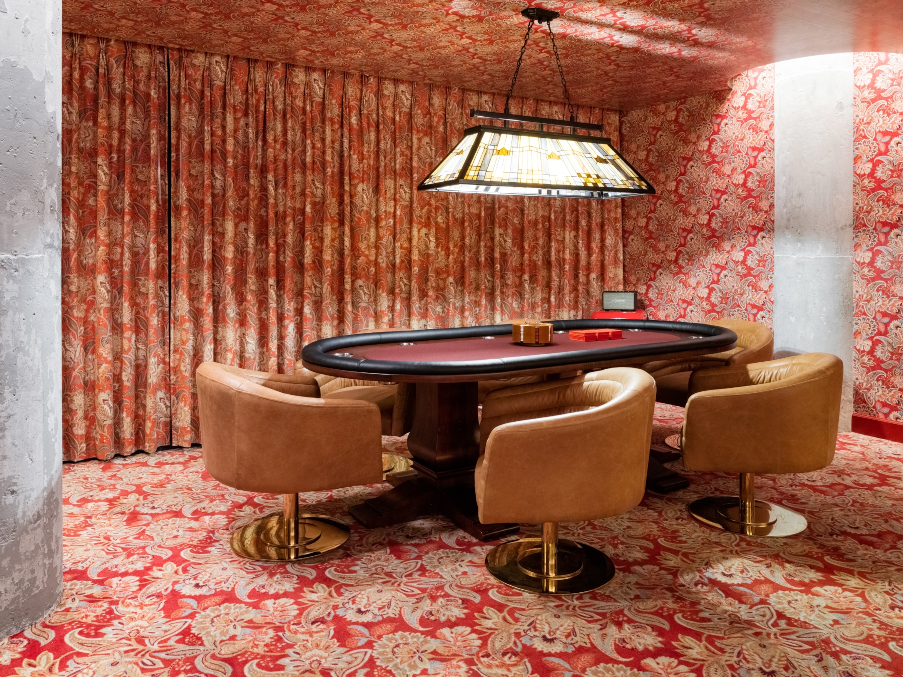 Długi, drewniany stół do pokera w pokoju pełnym tapet w czerwone wzory.