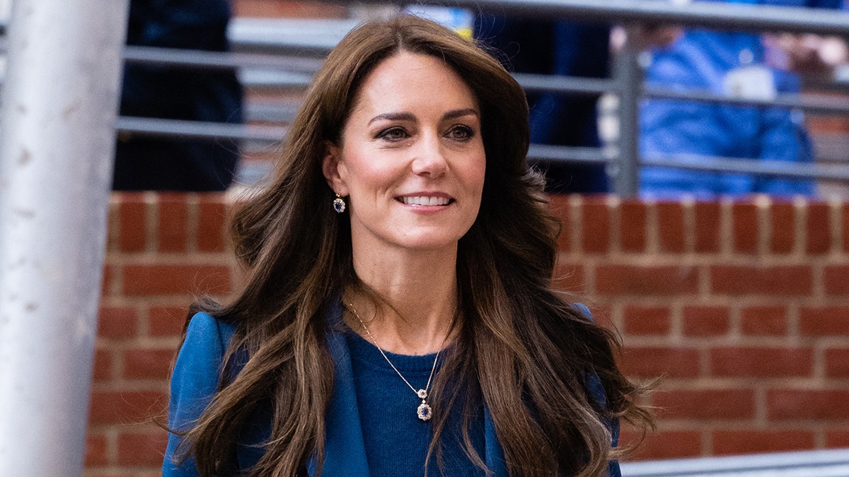 Kate Middleton uśmiecha się, ubrana w niebieski garnitur