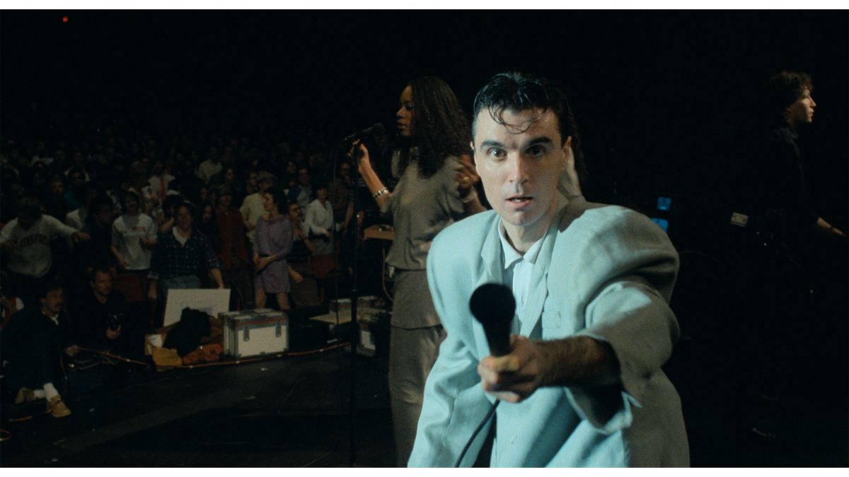 David Byrne, ubrany w swój charakterystyczny garnitur, trzyma mikrofon w stronę kamery w Stop Making Sense.