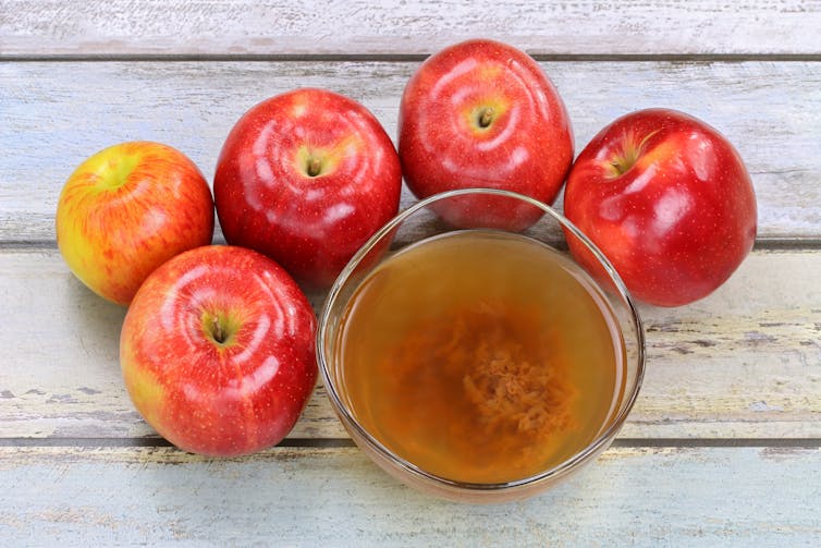 otwarta szklanka płynu z mętną substancją na dnie, otoczona jabłkami