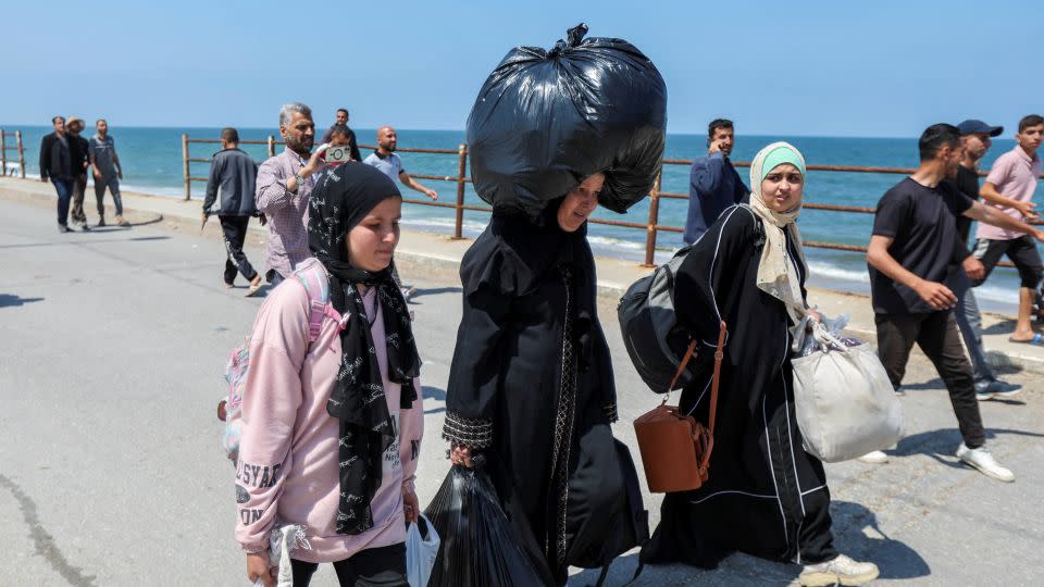 Um Mohammad (w środku) idzie drogą, niosąc na głowie ciężką torbę i dwie inne osoby w ramionach, kierując się w stronę północnej Gazy, 14 kwietnia 2024 r. – Ramadan Abed/Reuters