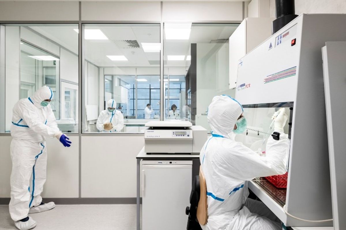 Naukowcy ubrani w biały sprzęt stwarzający zagrożenie biologiczne prowadzący badania w laboratorium.