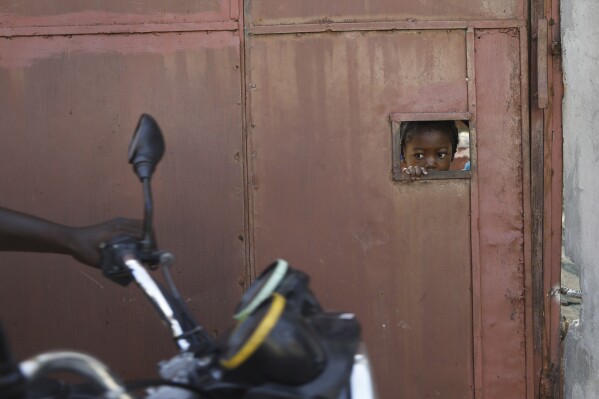 PLIK – Dziecko obserwuje przez otwór w bramce bezpieczeństwa, jak mieszkańcy uciekają ze swoich domów z powodu przemocy gangów, w Port-au-Prince, Haiti, 9 marca 2024 r. (AP Photo/Odelyn Joseph, plik)