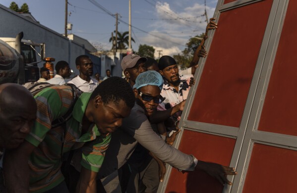 Sąsiedzi podnoszą metalową bramę podczas montażu barykady chroniącej przed gangami w dzielnicy Petion-Ville w Port-au-Prince na Haiti, sobota, 20 kwietnia 2024 r. (AP Photo/Ramon Espinosa)
