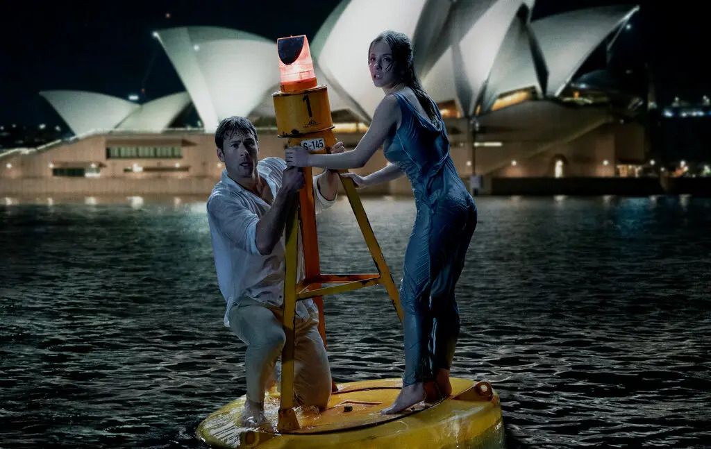 Mężczyzna i kobieta trzymają się boi w zatoce, na tle Opery w Sydney.