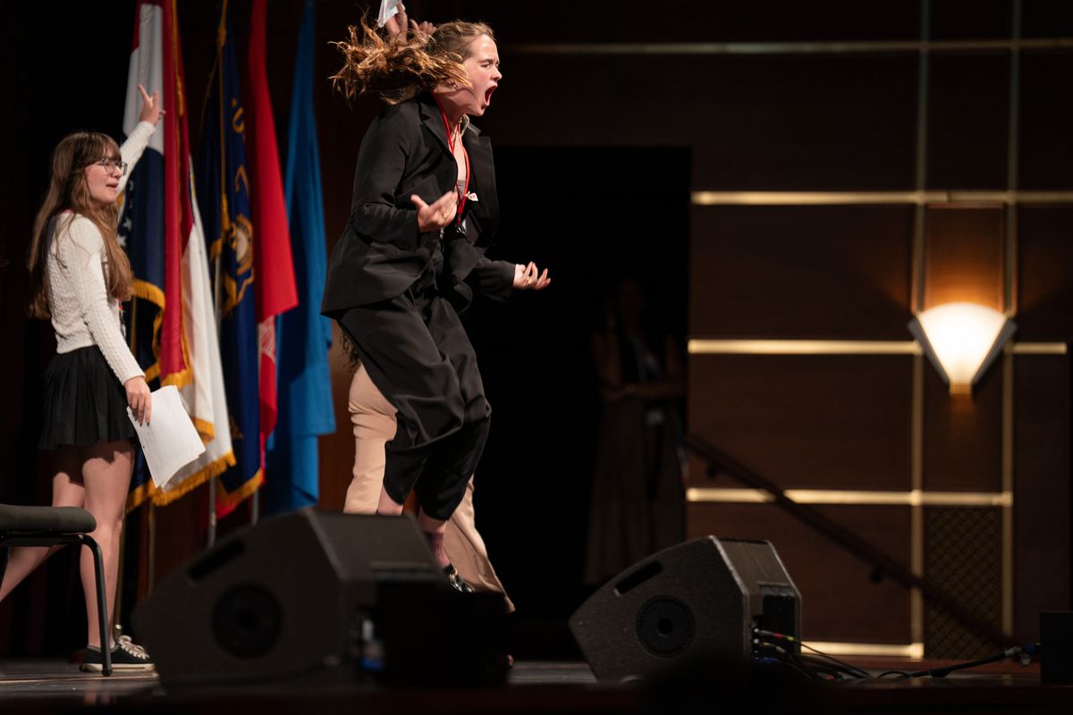 Cecilia Bartin, uczestniczka wydarzenia politycznego Girls State w Missouri w 2022 r., podskakuje w powietrze, krzycząc na scenie, wygłaszając przemówienie w filmie dokumentalnym Girls State
