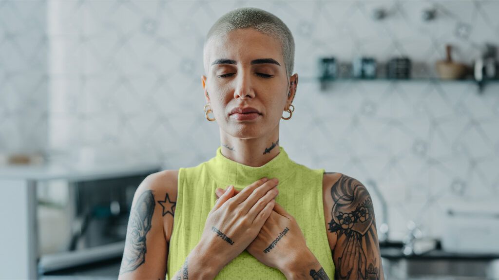 Kobieta zamyka oczy i trzyma się za klatkę piersiową podczas medytacji