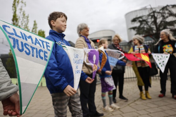 Ludzie demonstrują przed Europejskim Trybunałem Praw Człowieka we wtorek, 9 kwietnia 2024 r. w Strasburgu we wschodniej Francji.  Najwyższy europejski Trybunał Praw Człowieka wyda we wtorek orzeczenie w sprawie grupy przełomowych spraw dotyczących zmian klimatycznych, których celem jest zmuszenie krajów do wywiązania się z międzynarodowych zobowiązań w zakresie redukcji emisji gazów cieplarnianych.  Europejski Trybunał Praw Człowieka będzie wydawał orzeczenia w trzech sprawach wniesionych przez burmistrza Francji, sześć młodych Portugalczyków i ponad 2000 starszych Szwajcarek, które twierdzą, że ich rządy nie robią wystarczająco dużo, aby przeciwdziałać zmianom klimatycznym.  (AP Photo/Jean-Francois Badias)