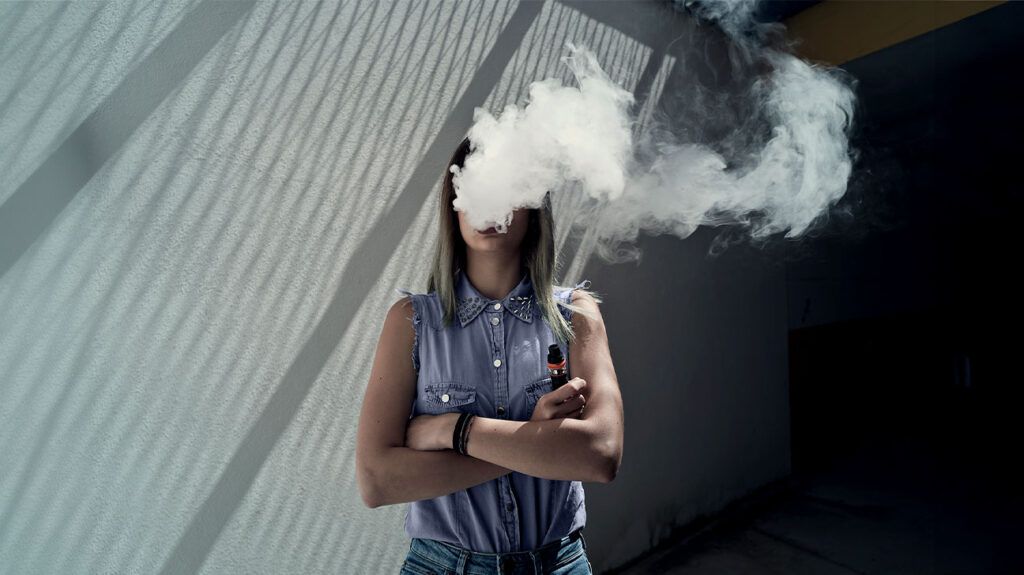 Kobieta wapuje, gdy chmura dymu zakrywa jej twarz