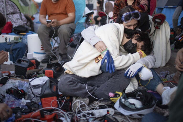 Propalestyńscy demonstranci obejmują się podczas ładowania urządzeń w obozowisku na terenie kampusu UCLA, środa, 1 maja 2024 r., Los Angeles.  (AP Photo/Ethan Swope)