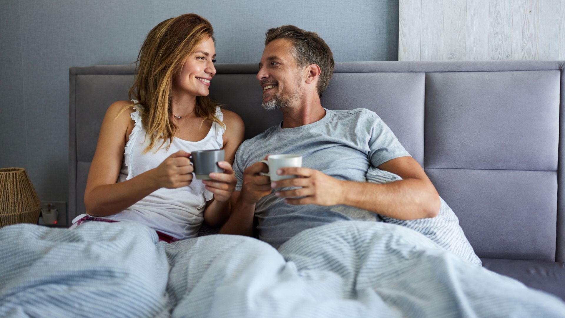 Para uśmiecha się pijąc kawę w łóżku