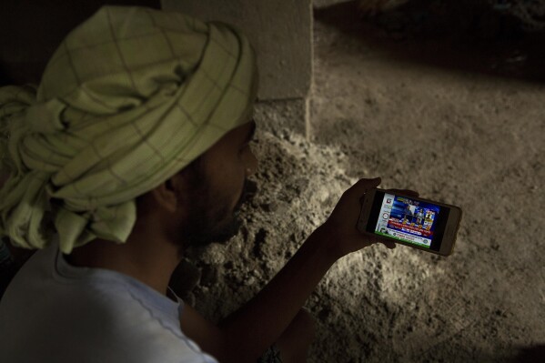 PLIK – Indyjski robotnik na placu budowy obserwuje na telefonie komórkowym trendy wyborcze w Gauhati w Indiach, 23 maja 2019 r. W Internecie rośnie liczba dezinformacji na temat wyborów w Indiach, ponieważ głosuje w najludniejszym kraju świata.  Kraj ma ogromny ekosystem internetowy z największą liczbą użytkowników WhatsApp i YouTube na świecie.  (AP Photo/Anupam Nath, plik)