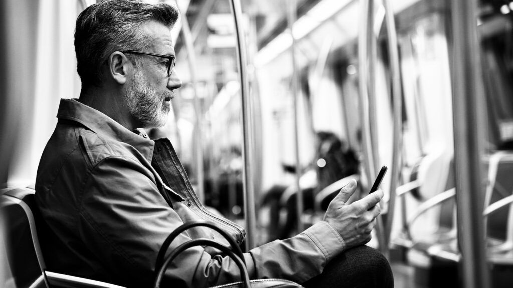 Starszy mężczyzna w okularach i kurtce czyta na telefonie komórkowym podczas dojazdów metrem