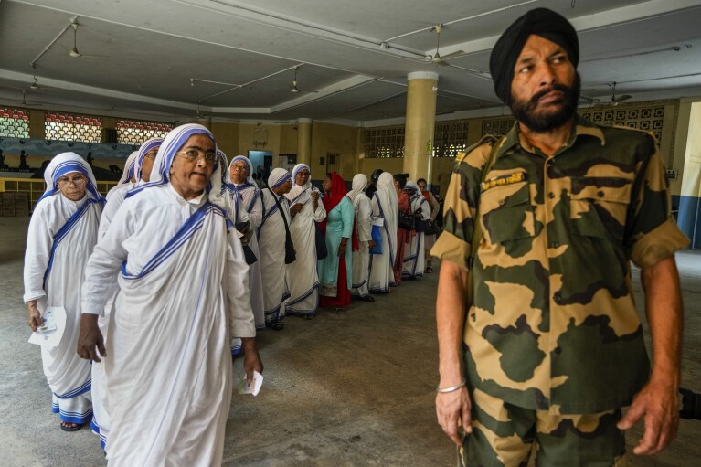 Indyjski żołnierz sił paramilitarnych stoi na straży, gdy zakonnice Misjonarek Miłości, zakonu założonego przez św. Teresę, stoją w kolejce, aby oddać głos w ostatniej turze sześciotygodniowych wyborów krajowych w Kalkucie w Indiach, Sobota, 1 czerwca 2024 r. (AP Photo/Bikas Das)