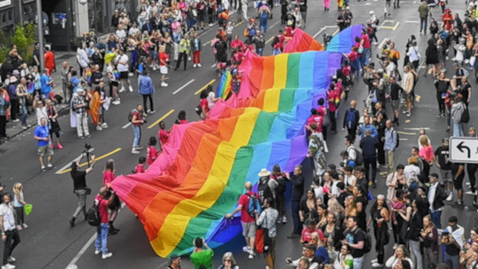 Wiele osób macha ogromną tęczową flagą.  Wielki tłum spaceruje ulicą miasta.  Zabawny symbol społeczności LGBT.  Zatrzymaj koncepcję homofobii.  Święto miesiąca radości.  Bi geje idą na imprezę z okazji Dnia Miłości csd.  Festiwal kultury queer.
