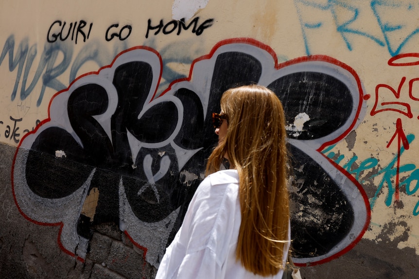 Kobieta przechodzi obok graffiti na ścianie w Hiszpanii, które mówi: "Guiri idź do domu" co przekłada się na "turysta idź do domu".