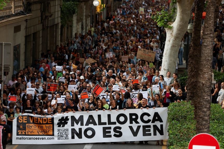 Ludzie trzymają transparent z napisem "Majorka nie jest na sprzedaż"biorąc udział w proteście przeciwko masowej turystyce.