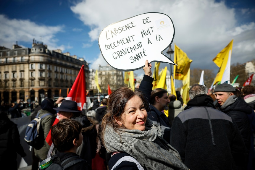 Protestujący w Paryżu trzyma tabliczkę w języku francuskim z napisem: "Brak mieszkania poważnie szkodzi zdrowiu".