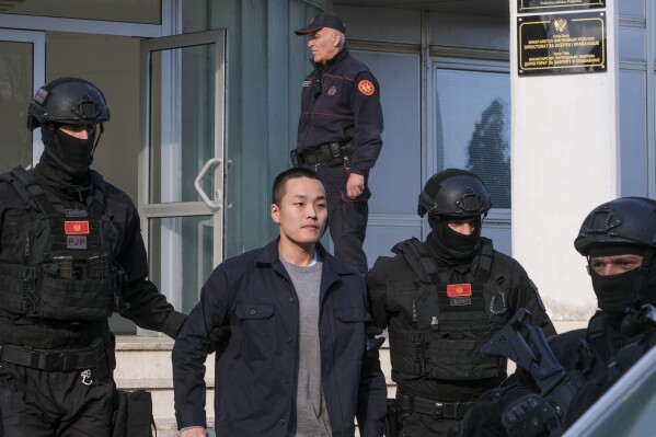 Czarnogórscy policjanci eskortują obywatela Korei Południowej, założyciela Terraform Labs Do Kwona w stolicy Czarnogóry Podgoricy, sobota, 23 marca 2024 r. Do Kwon został w sobotę przeniesiony z więzienia, gdzie odbywał 4-miesięczny wyrok za używanie fałszywego paszportu, do ośrodek dla obcokrajowców oczekujących na jego ogłoszoną ekstradycję do rodzinnej Korei Południowej.  (AP Photo/Risto Bozovic)