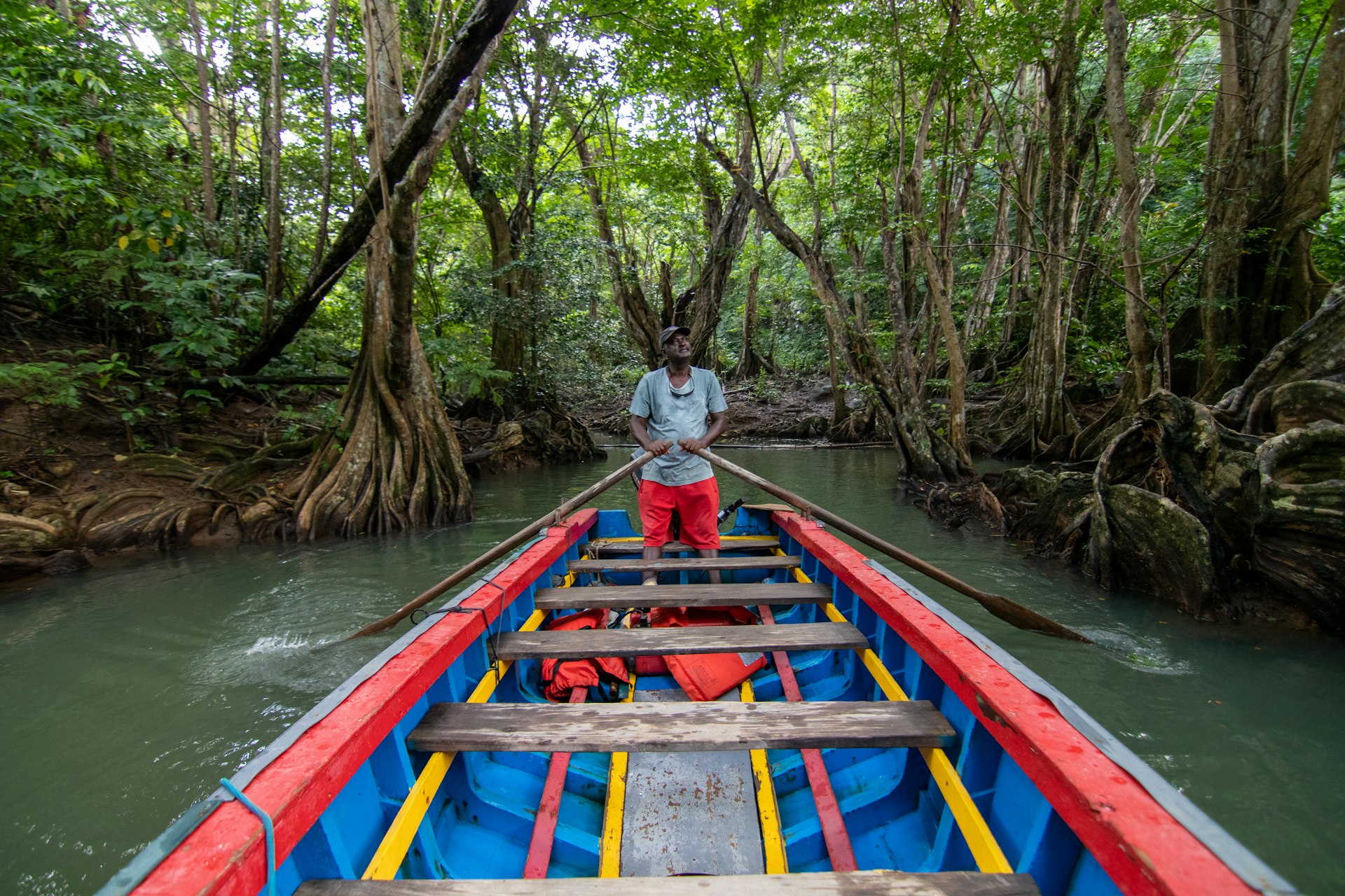 Czerwona łódź z mężczyzną stojącym na dziobie, płynąca wzdłuż rzeki Indian na Dominice