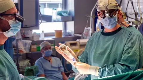 BBC Zdjęcie lekarza trzymającego urządzenie do fali uderzeniowej podczas operacji, ubranego w fartuch, maskę i rękawiczki