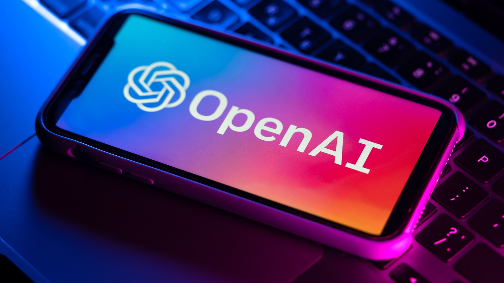 Logo OpenAI na telefonie umieszczonym na klawiaturze laptopa