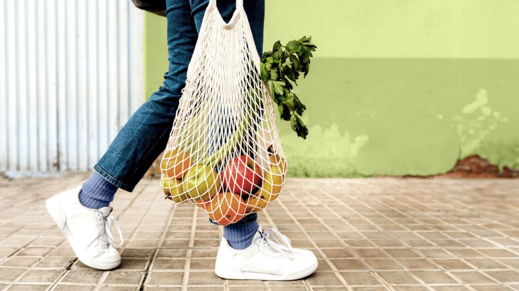 Osoba trzymająca torbę świeżych owoców i warzyw idzie chodnikiem