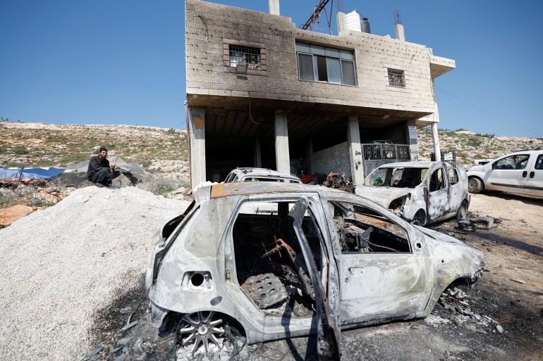 Palestyńczyk siedzi w pobliżu uszkodzonego domu i uszkodzonych samochodów po tym, jak izraelscy osadnicy zaatakowali wioskę al-Mughayyer na okupowanym przez Izrael Zachodnim Brzegu, 13 kwietnia 2024 r.