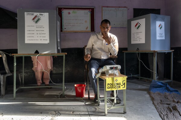Urzędnik wyborczy patrzy na swoje urządzenie w celu potwierdzenia, gdy wyborca ​​oddaje swój głos w wyborach uzupełniających po głosowaniu w siódmej i ostatniej turze głosowania w wyborach krajowych w Indiach w Dharamsali, sobota, 1 czerwca 2024 r. (AP Photo/Ashwini Bhatia )