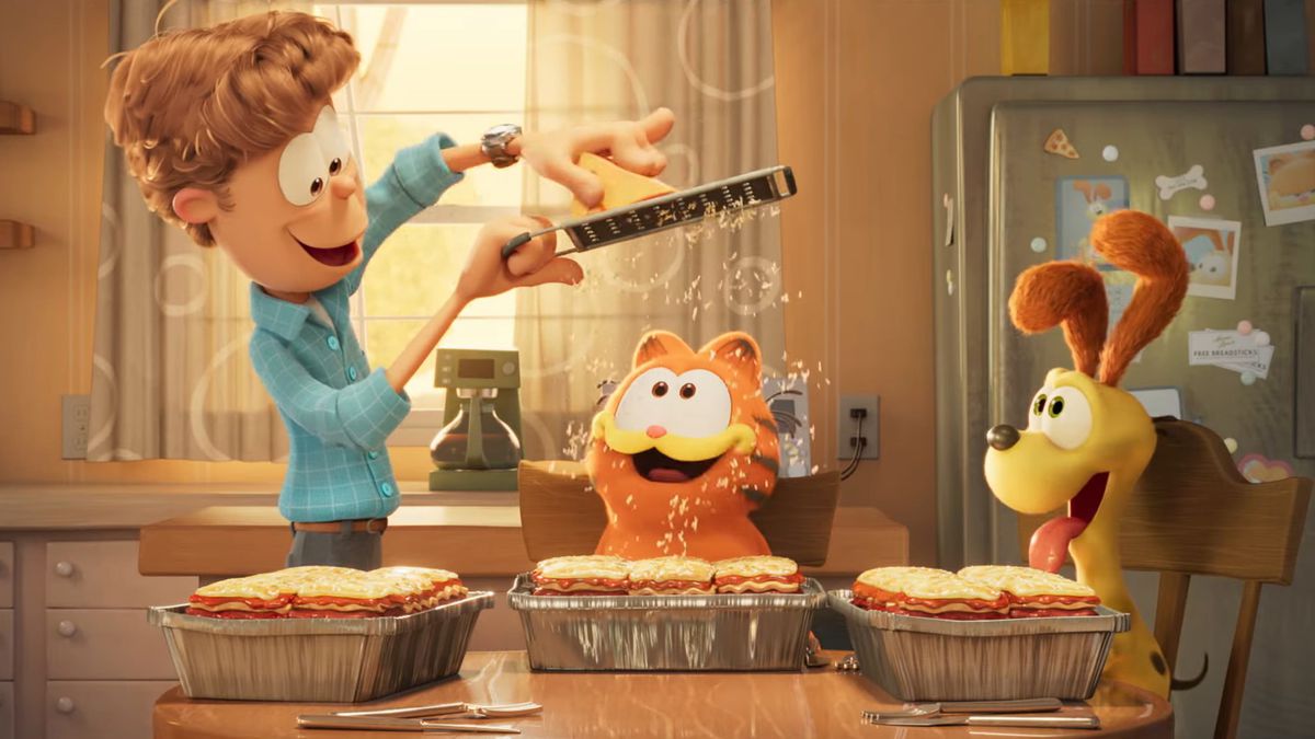 Jon Arbuckle ściera parmezan na lasagne Garfielda, podczas gdy Odie to obserwuje na zdjęciu z filmu Garfield