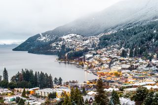 Domy oświetlone o zmierzchu na tle pokrytych śniegiem drzew w Queenstown w Nowej Zelandii