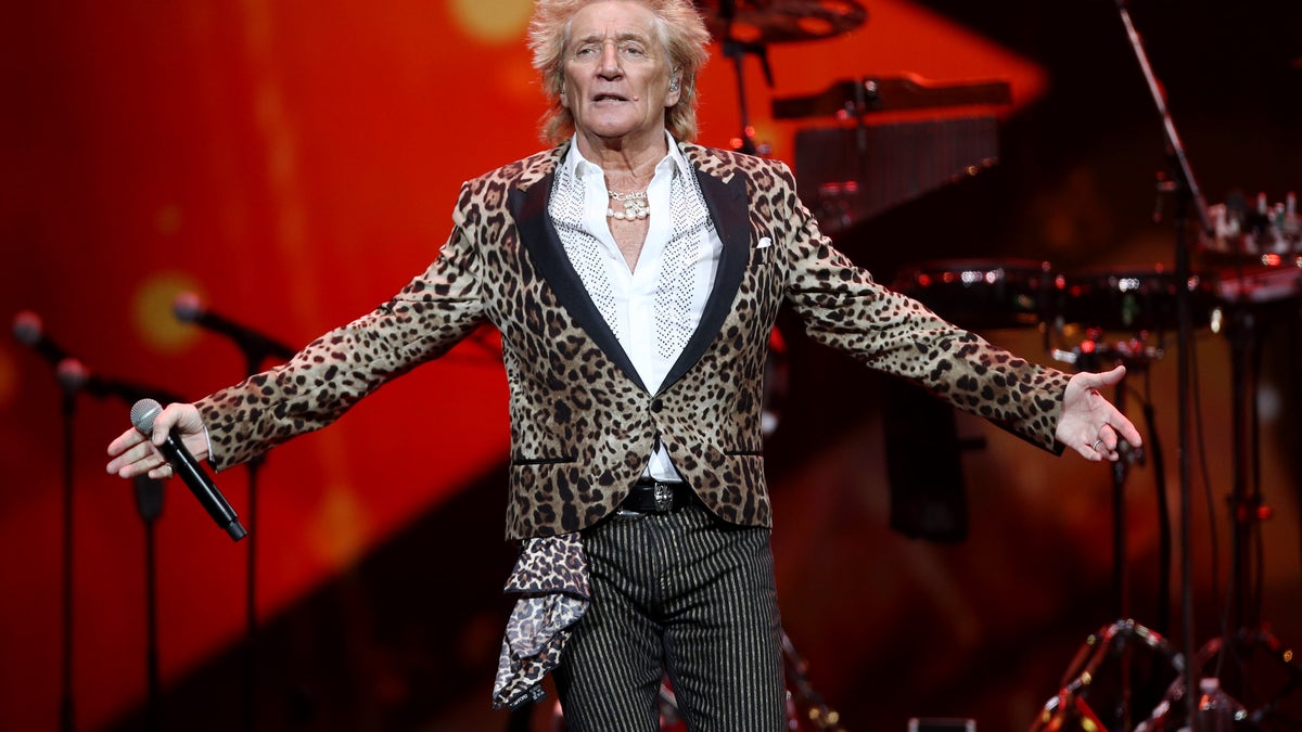 Rod Stewart z szeroko rozłożonymi ramionami na scenie