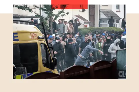 Getty Images Tłum protestujących mężczyzn za policyjnym furgonetką. Jeden mężczyzna na pierwszym planie ma na sobie czarną osłonę twarzy, niebieski dres i spodenki. Wygląda, jakby czymś rzucał.