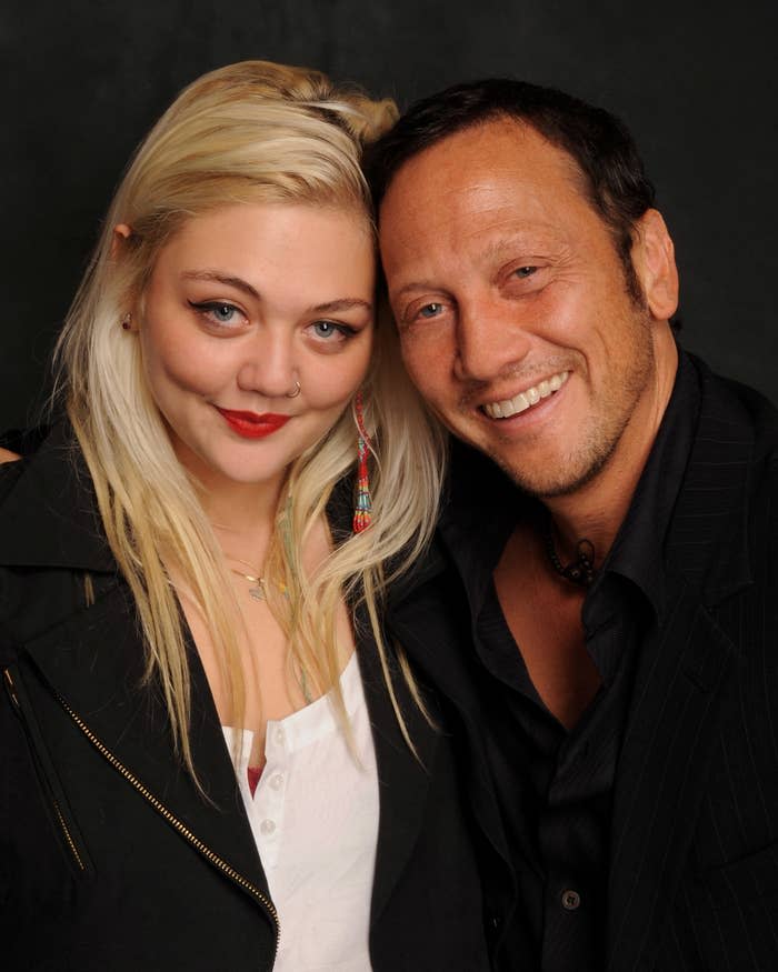 Elle King i Rob Schneider uśmiechnięci, Rob Schneider ubrany w ciemny garnitur, a Elle King w luźną bluzkę i ciemną kurtkę