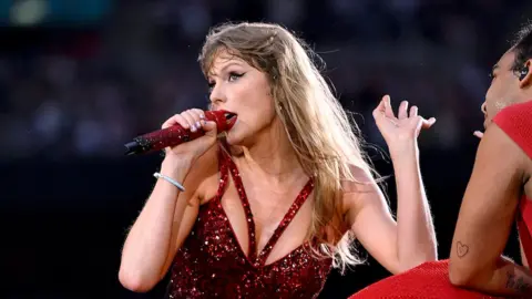 Getty Images Taylor Swift występująca w czerwonym topie z pasującym mikrofonem.