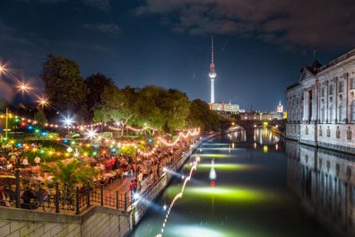 Ludzie tańczą na letniej imprezie na plaży Strandbar w pobliżu rzeki Sprewy na Wyspie Muzeów ze słynną wieżą telewizyjną w tle nocą, Berlin, Niemcy