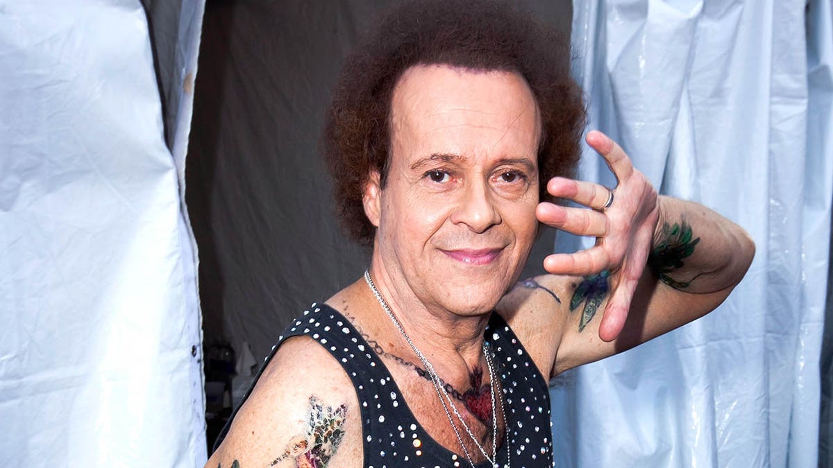 Richard Simmons uśmiecha się i podnosi rękę