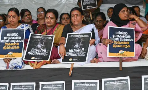 Arun Chandra Bose/BBC Kobiety z Mahila Congress siedzą na proteście, trzymają plakaty i domagają się podjęcia działań w związku ze sprawozdaniem komisji Hema w Kochi w piątek